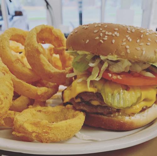 A juicy cheeseburger with lettuce, tomato, and pickles, served with crispy onion rings on the side.