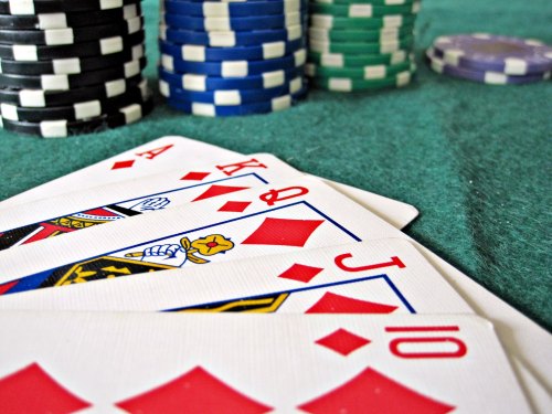 A close-up of playing cards showing Ace, King, Queen, Jack, and Ten of diamonds, with stacks of poker chips in the background.