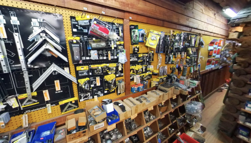 A well-organized hardware store wall displaying various tools, fasteners, and supplies on pegboards and in bins.
