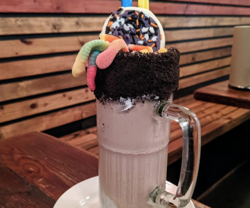A tall glass filled with a creamy milkshake, topped with colorful candies, sprinkles, and crushed cookies.