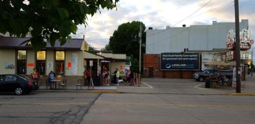 A street scene showing people outside a restaurant, with a nearby sign for Lakeland Care and a cloudy sky.