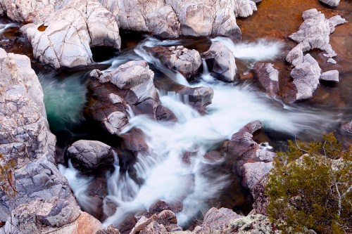 Aerial view of a rocky riverbed with flowing water, surrounded by smooth stones and greenery.