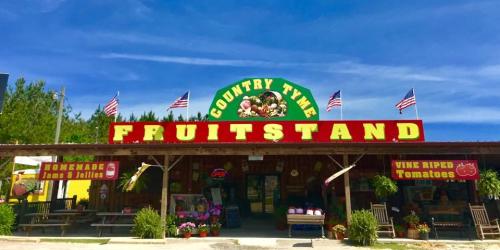 A colorful fruit stand with a sign reading "Country Time Fruitstand," featuring flags and displays of produce.