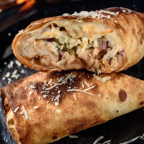 A close-up of a grilled burrito filled with meat, cheese, and vegetables, garnished with shredded cheese on top.
