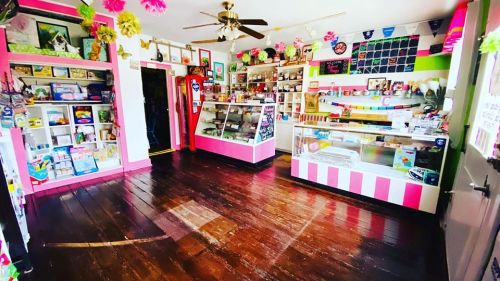 A colorful shop interior with pink accents, display cases, shelves of items, and a wooden floor.