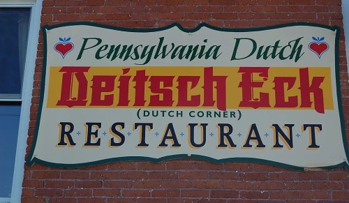 Sign for "Pennsylvania Dutch Deitsch Eck Restaurant" featuring colorful lettering on a brick background.