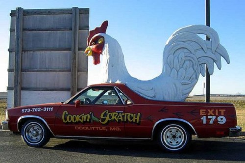 A red car with a giant chicken sculpture on top, advertising "Cookin' from Scratch" in Doolittle, MO.
