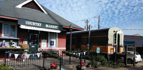 A quaint country market with a vintage truck parked outside, surrounded by festive decorations and a blue sky.