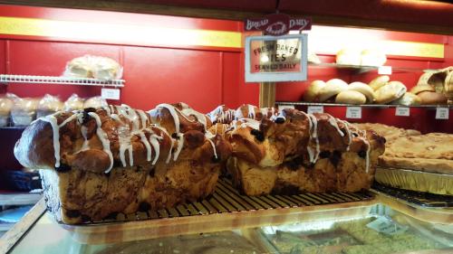 Freshly baked sweet bread loaves drizzled with icing, displayed in a bakery with various breads in the background.
