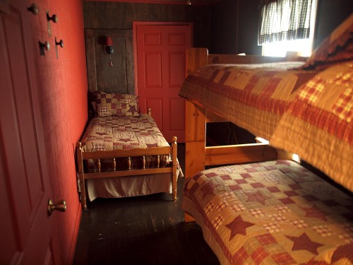 Cozy bedroom with a red wall, featuring a single bed and a bunk bed, both with patterned quilts.
