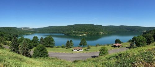 A panoramic view of a serene lake surrounded by lush green hills under a clear blue sky.