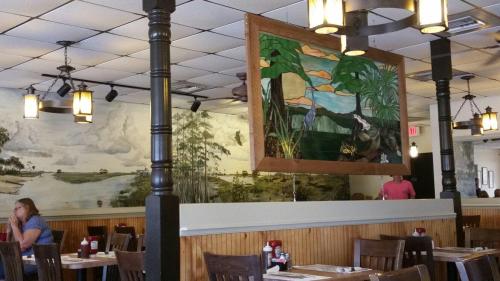 Interior of a restaurant featuring a large stained glass artwork and scenic murals on the walls, with wooden tables.