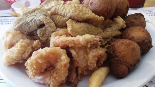A plate of assorted fried seafood, including shrimp, fish fillets, and hushpuppies, served with fries.
