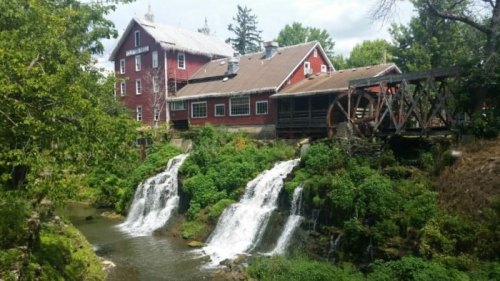A red barn beside a watermill, with cascading waterfalls and lush greenery surrounding the scene.