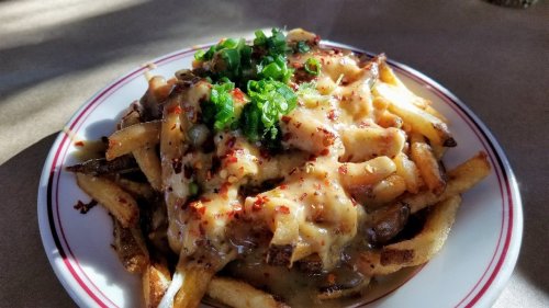 A plate of loaded fries topped with cheese sauce, green onions, and red pepper flakes.