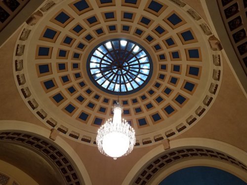 A circular ceiling with a large skylight and an ornate chandelier hanging below, featuring geometric patterns.