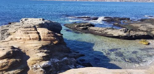 Rocky coastline with clear blue water and gentle waves, creating a serene coastal landscape.