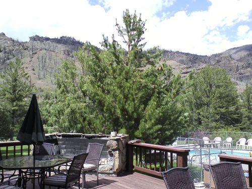 A scenic view from a deck featuring a pool, trees, and mountains under a partly cloudy sky.