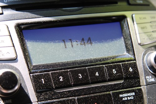 Close-up of a car radio display showing the time 11:44, with visible dust on the surface.