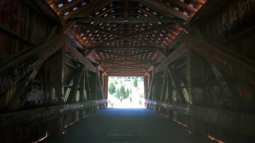 View inside a wooden covered bridge, showcasing a rustic interior with beams and light streaming through the openings.