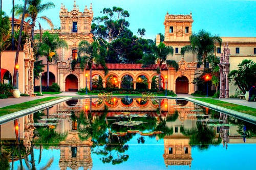 A serene garden scene featuring a reflecting pond, palm trees, and ornate buildings in a tranquil setting.