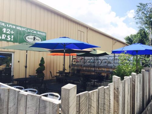 Outdoor seating area with colorful umbrellas, surrounded by a wooden fence and a building in the background.