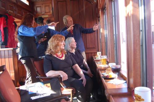 A group of people inside a wooden train car, enjoying drinks and snacks while looking out the window.