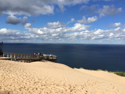 A sandy beach with a wooden pier overlooking a calm blue ocean under a partly cloudy sky.