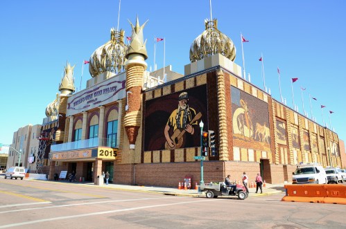 A large, ornate building with golden domes and a mural, set against a clear blue sky. Traffic signals and vehicles are visible.
