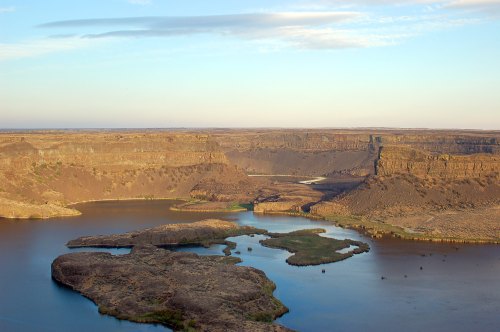 A scenic view of a river winding through rocky canyons and islands under a clear blue sky.