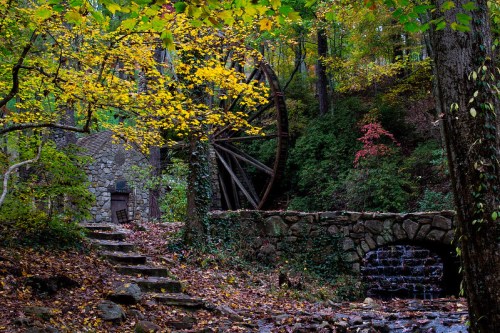 A scenic view of a stone mill with a water wheel, surrounded by colorful autumn leaves and a gentle stream.