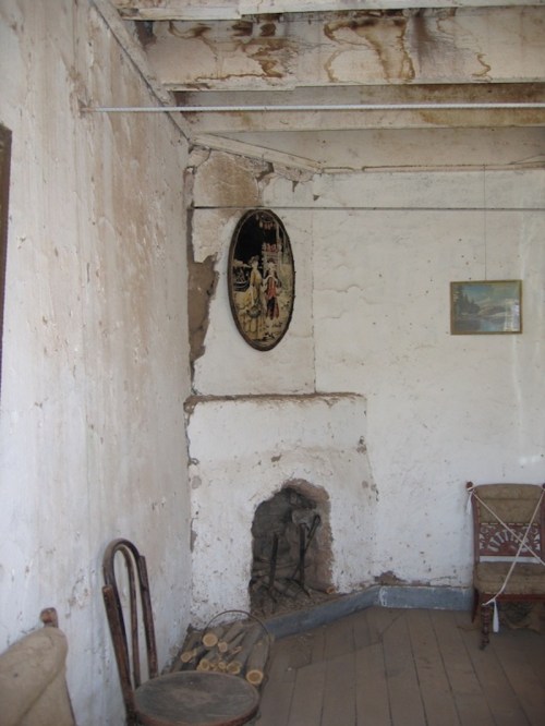 Interior of a rustic room with peeling walls, a fireplace, and vintage decor, including a framed picture and a mirror.