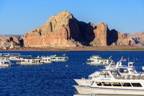Boats docked on a lake with a backdrop of rugged red rock formations and clear blue skies.