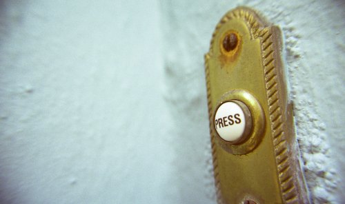 Close-up of a vintage brass doorbell button with the word "PRESS" on a textured wall.