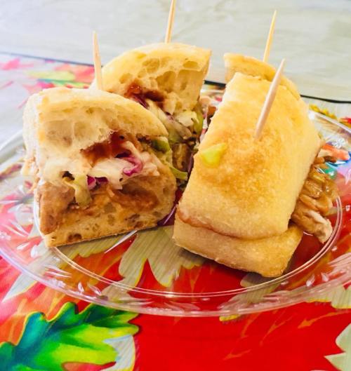 A close-up of a sandwich with pulled meat and coleslaw, cut in half and held together with toothpicks on a colorful table.