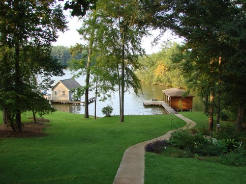 A serene lakeside view with two wooden docks, surrounded by lush greenery and trees under a clear sky.