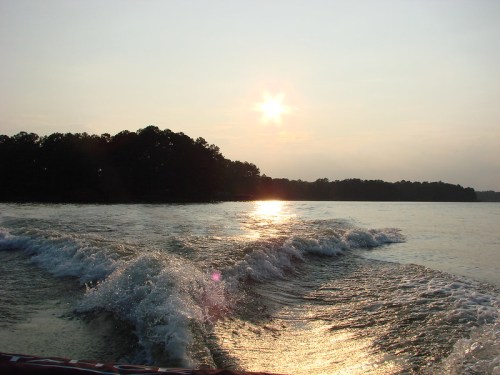 Sunset over a calm lake, with gentle waves and silhouettes of trees along the shore.