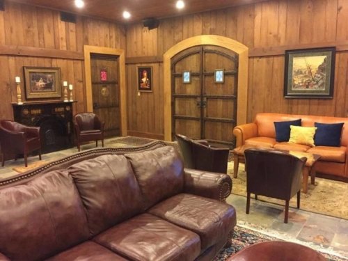 Cozy lounge with wooden walls, leather sofas, armchairs, and framed artwork, creating a warm, inviting atmosphere.