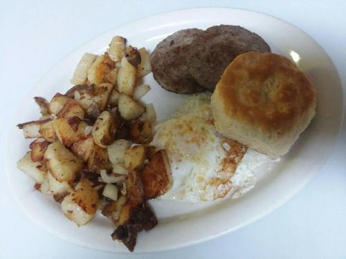 A plate of breakfast featuring fried eggs, sausage patties, crispy potatoes, and a biscuit.