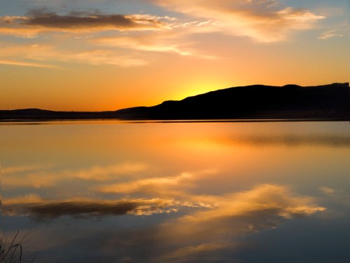 A serene sunset over a calm lake, with vibrant orange and yellow hues reflecting on the water's surface.