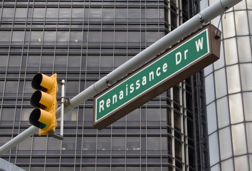 Street sign for Renaissance Dr W with a yellow traffic light in front of a modern building.