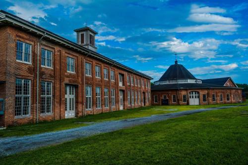Historic brick buildings with large windows under a blue sky, featuring a round roof structure in the background.