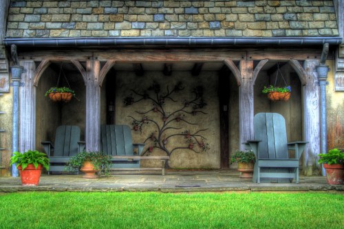 A cozy porch with two Adirondack chairs, potted plants, and decorative wall art under a wooden roof.