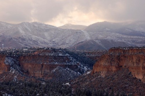 Snow-covered mountains and cliffs under a cloudy sky, with a hint of sunlight breaking through the clouds.