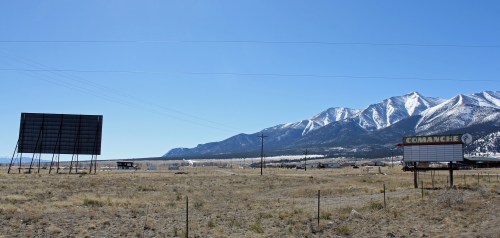 A barren landscape with two billboards and snow-capped mountains in the background under a clear blue sky.