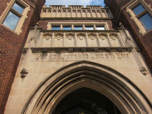Close-up of a historic building entrance with the inscription "Live to Learn and Learn to Live" above the archway.