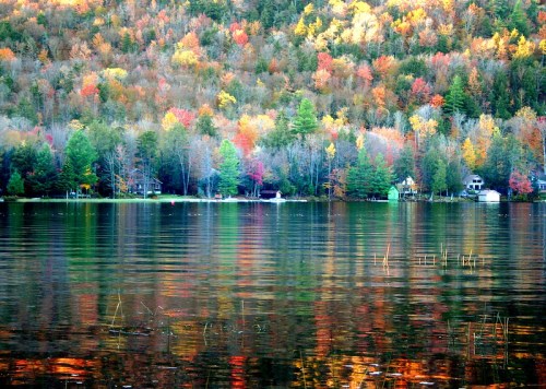 A serene lake reflecting vibrant autumn foliage and cozy cabins along the shore.