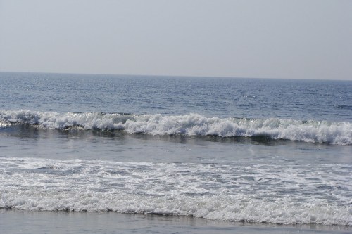 Waves gently rolling onto a sandy beach under a clear blue sky.