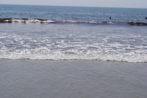 A serene beach scene with gentle waves lapping at the shore under a clear blue sky.