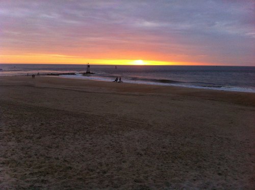 A serene beach at sunset, with gentle waves and silhouettes of people walking along the shore.